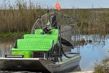 Airboat with bright green seats parked near marshland in a waterway.